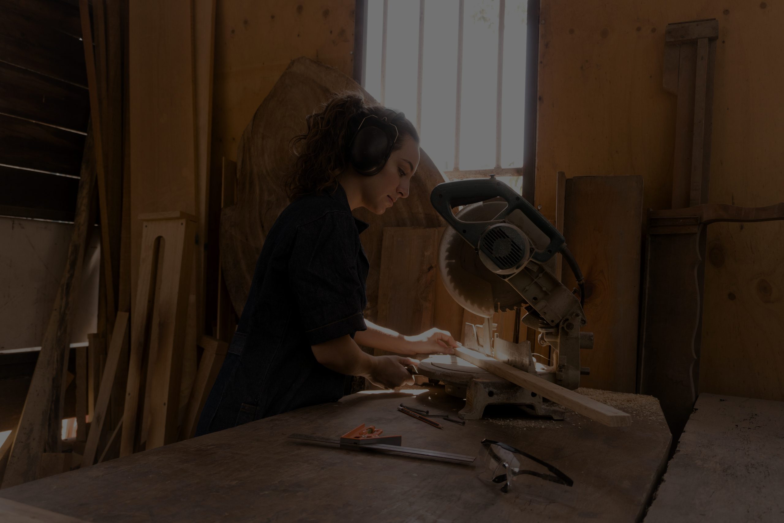 A joiner wearing ear defenders cutting timber at a mitre saw in a workshop