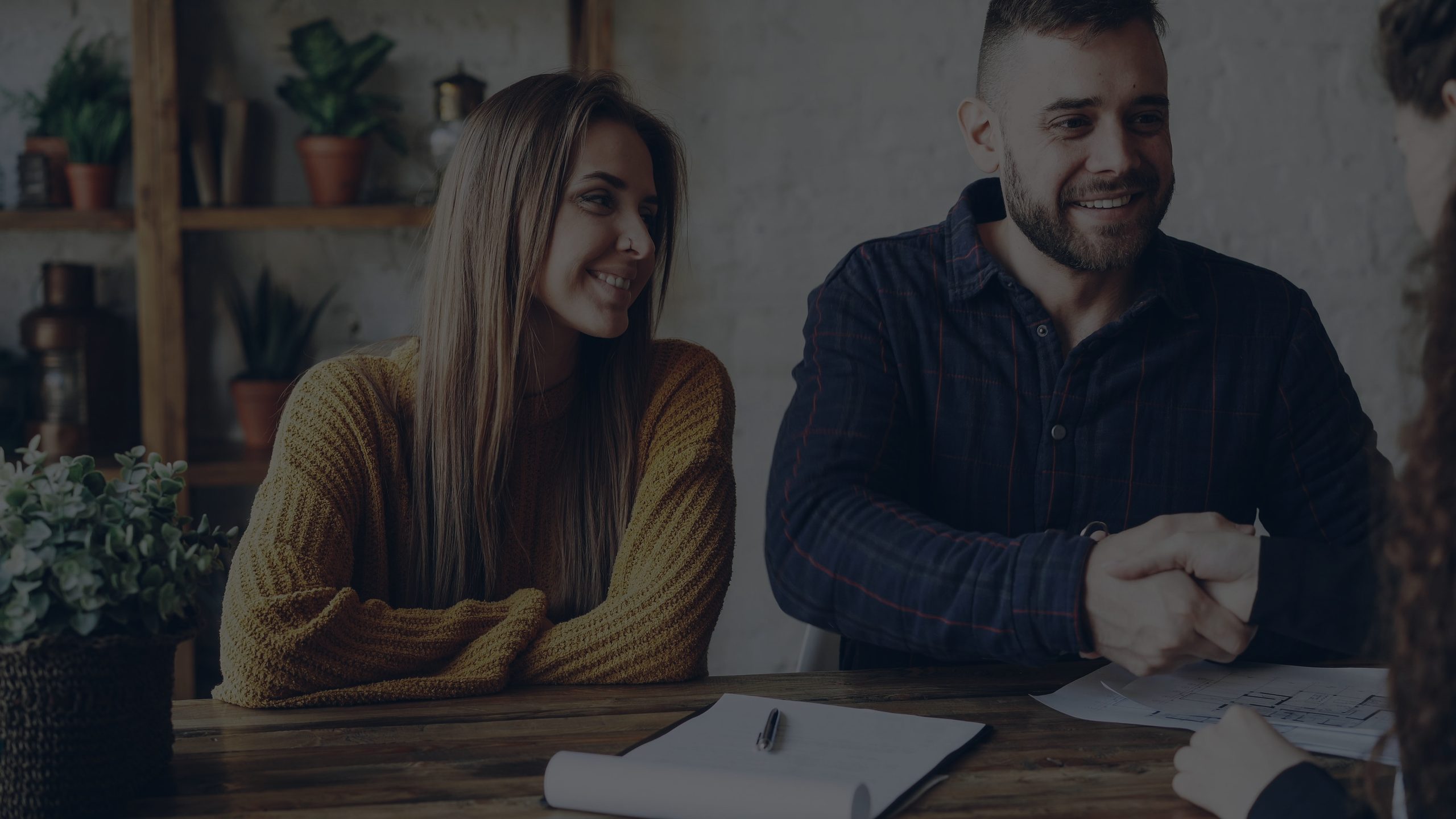 A smiling couple shaking hands with a contractor across a table with plans on it